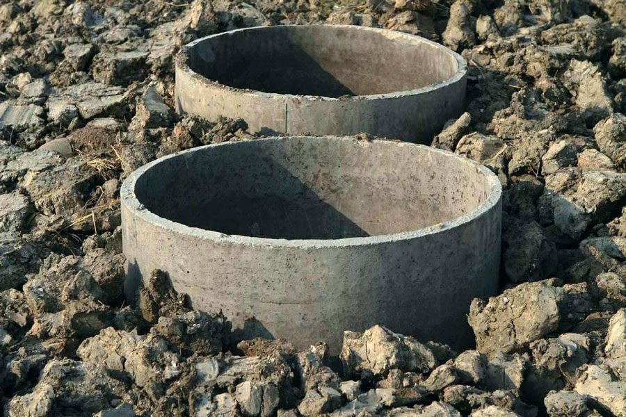 Due anelli di cemento circolari, parzialmente affondati in un terreno arido e disordinato, circondati da roccia e macerie.