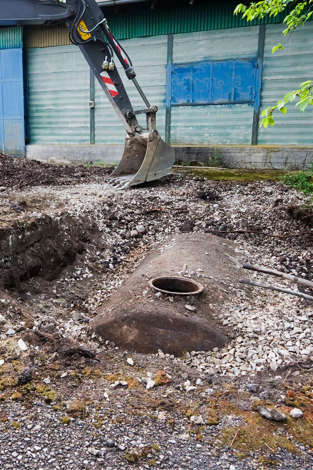 Un'escavatrice sta scavando nel terreno vicino a un serbatoio sotterraneo arrugginito. Intorno, rocce e detriti.
