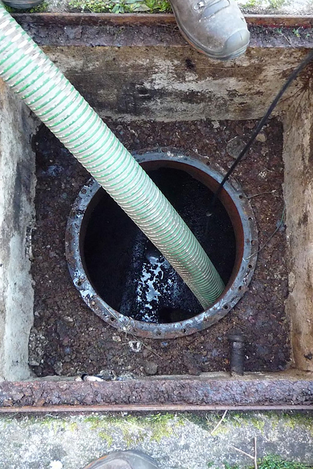 Immagine di un pozzetto visibile da un'apertura circolare, con un tubo verde che penetra all'interno. Il fondo è scuro e umido.